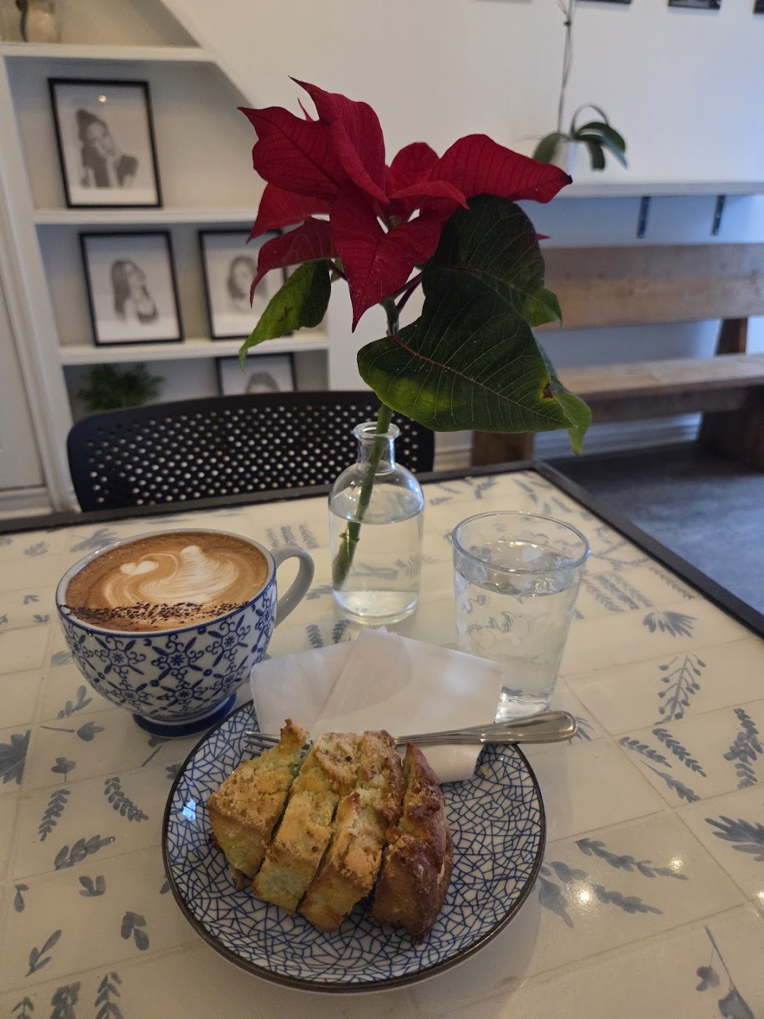Latte with artisan cake, fresh flower and water served at Moments cafe table